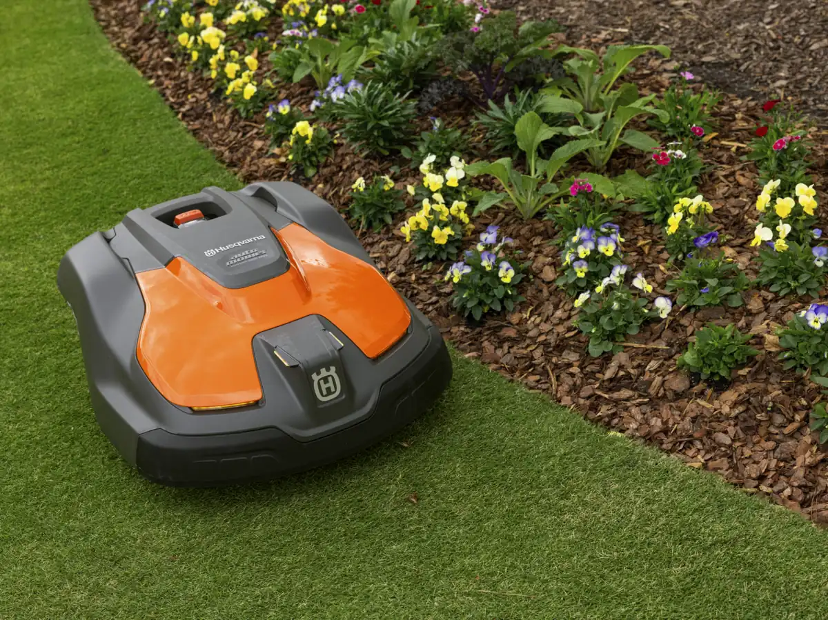 A robotic mower cutting a striped commercial lawn beside planted beds