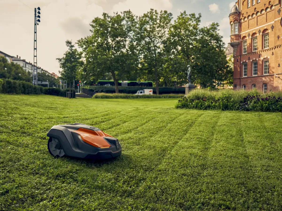 A robotic mower on a striped lawn in front of a large institutional building