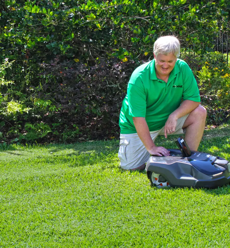 Scott Parker, owner of GreenMow Robotics, kneeling beside a robotic mower on a lawn
